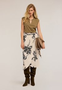 Olivově zelený top bez rukávů s detailem ve tvaru klíčové díry, zkombinovaný se smetanovou sukní s černými květinovými vzory a kozačkami z hnědého semiše po kolena.