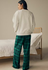 Ljust grå oversized sweatshirt tillsammans med gröna rutiga pyjamasbyxor. Tyget är mjukt, med en avslappnad passform och ribbade ärmslut.