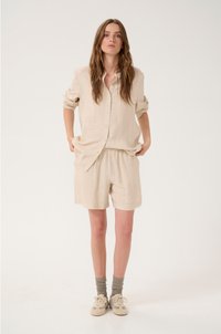 Beige shirt met korte mouwen, met een knoopsluiting aan de voorkant en bijpassende shorts. Zacht, gestructureerd fabric met een relaxte pasvorm en een licht gekreukt uiterlijk.