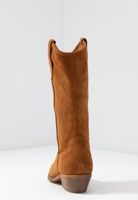 Brązowy zamszowy but w stylu westernowym z niskim obcasem, dekoracyjnym wytłaczanym motywem błyskawicy po bokach i zaokrąglonym noskiem.