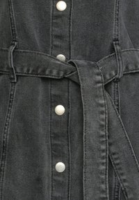 Czarna kurtka dżinsowa z srebrnymi guzikami, z pasem w talii oraz teksturowanym materiałem z pionowymi przeszyciami.