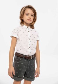 Vit kortärmad skjorta med små djurmotiv och knäppning, i kombination med grå upprullade shorts med en subtilt mönster och flätat bälte.