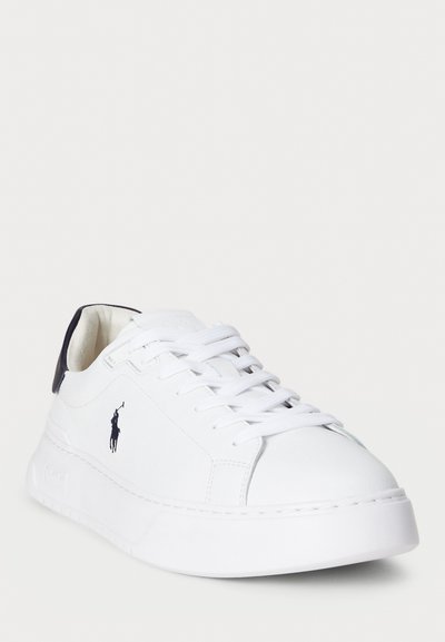 Hvit sneakers med teksturert skinnoverside, rund tå og flat såle. Har hvite lisser og en marineblå aksent på hælen. Polo-logo på siden.