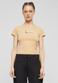 Beige bomull t-skjorte med kort erm og rund hals, med et trykt design på brystområdet. Brukt med svarte joggebukser med snøring.