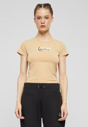 Beige bomull t-skjorte med kort erm og rund hals, med et trykt design på brystområdet. Brukt med svarte joggebukser med snøring.