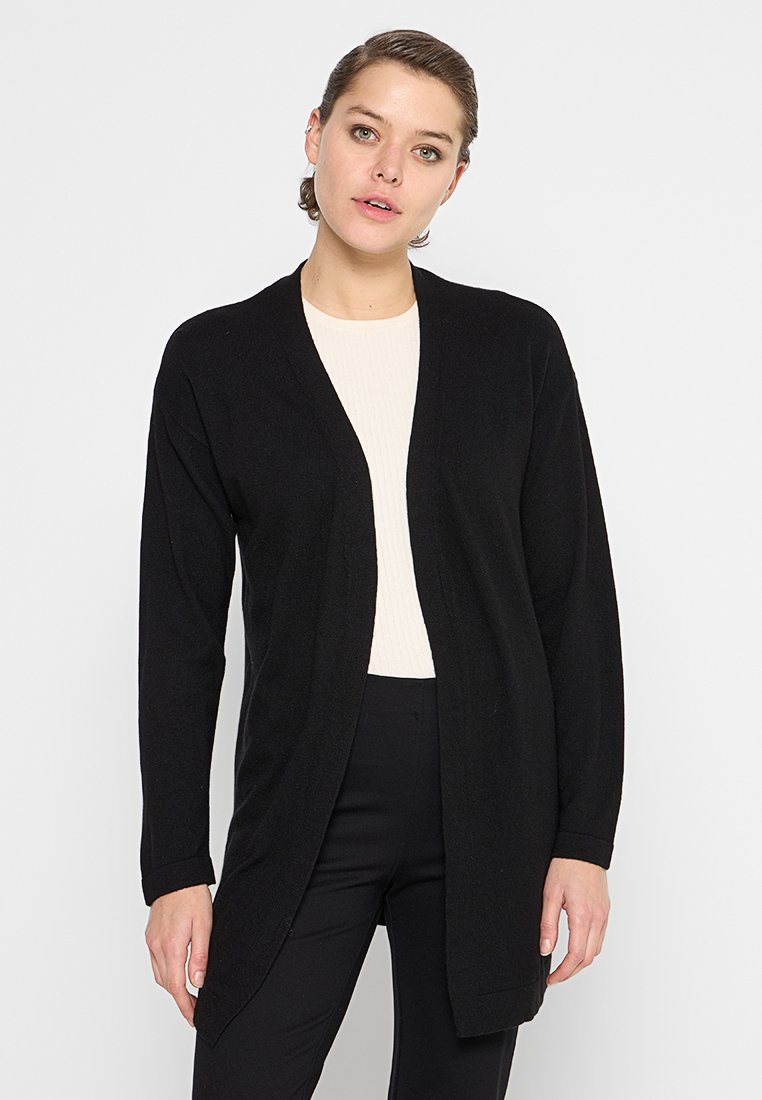Czarny kardigan z otwartym przodem, długimi rękawami i miękką teksturą. Nosi się go na jasnej bluzce, stylizowany z czarnymi spodniami.