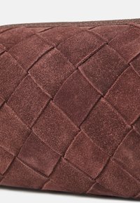 Borsa a tracolla in suede marrone con un motivo intrecciato, che mostra una superficie testurizzata con quadrati e forme rettangolari in una tonalità ricca.
