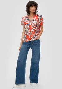 Rote kurzärmelige Bluse mit weißen und blauen Blumenmustern, kombiniert mit weiten blauen Jeans und weißen Sneakers, in lässiger Passform.
