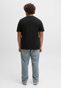 Schwarzes Baumwoll-T-Shirt mit kurzen Ärmeln, Rundhalsausschnitt und geradem Schnitt, kombiniert mit hellblauen Jeans und weißen Sneakers.