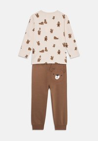 To-delt børnepyjamas sæt: cremet langærmet top med brunt bjørneprint og brune bukser med et bjørneansigt på baglommen. 100% bomulds materiale.