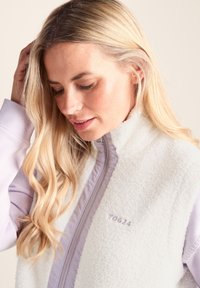 White fleece vest with a high collar, featuring a lavender zipper and accents. Includes a subtle logo on the chest and long purple sleeves.