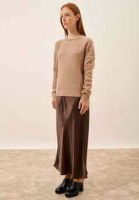 Beige gebreide trui met een textuurpatroon, gecombineerd met een donkerbruine satijnen rok. Model draagt zwarte plateau schoenen. Eenvoudig en elegant ontwerp.