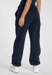 Marineblaue Jogginghosen mit lockerer Passform, elastischem Bund, Seitentaschen und gerippten Knöchelbündchen, kombiniert mit weißen Turnschuhen.