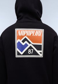 Sudadera negra con capucha que presenta un gran gráfico en la parte posterior con el texto "NAPAPIJRI" en blanco y naranja, un diseño de montaña azul y el número "87".