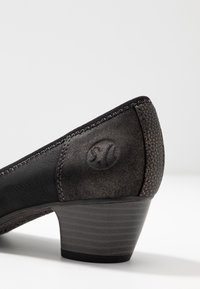 Černá kožená špičatá botička se strukturovaným zadním dílem, jemným logem a zaobleným špičatým designem, s nízkým, vrstveným podpatkem pro stabilitu.