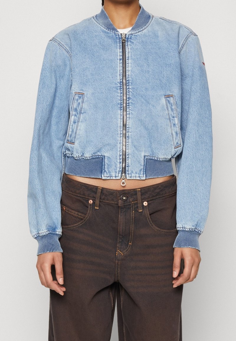 Svetle modrá džínová bomber bunda s žebrovanými manžetami a lemem, s předním zipem a dvěma bočními kapsami. Kombinováno s tmavě hnědými džíny.