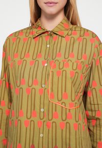 Πράσινο πουκάμισο με κουμπιά, διακοσμημένο με λουλουδάτο σχέδιο από κόκκινες τουλίπες και καφέ γραμμές, τσέπη στο στήθος με πορτοκαλί περιθώριο και κλασικό γιακά.