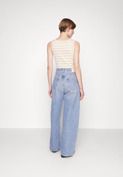 Débardeur beige rayé associé à un jean large taille haute bleu clair. Texture lisse et design décontracté avec poches arrière et ourlet brut.