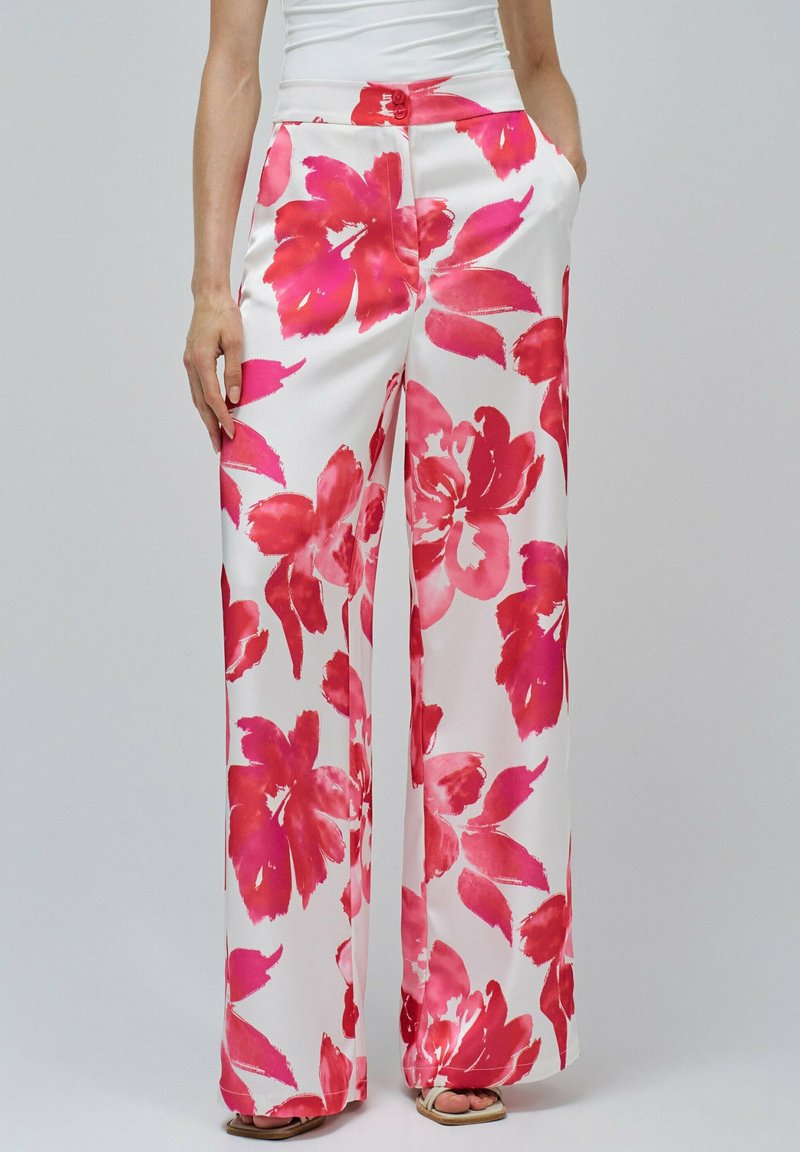 Pantalons larges à fleurs en tissu blanc, ornés de grands motifs de fleurs roses et rouges, avec des poches latérales et une fermeture à bouton à la taille.
