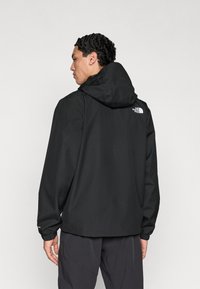 Μαύρο σακάκι με κουκούλα από υλικό soft-shell. Διαθέτει ελαστικές μανσέτες, λογότυπο στην πλάτη και άνετη, χαλαρή εφαρμογή για άνεση και ελευθερία κινήσεων.