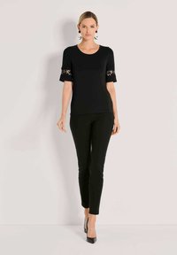 Black short-sleeve top with lace accents on sleeves, paired with fitted black pants and black heels, creating a sleek monochromatic look.