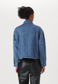 Quiltet denimjakke i blå med krage, synlig søm og elastisk bunnkant. Båret med tettsittende svarte bukser.