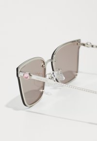Ruudukujulised prillid tumedate pruunide läätsedega, hõbedasest metallraamist, kergelt tekstureeritud tempeldest ja roosa Swarovski kristalli aktsendiga hingedel.