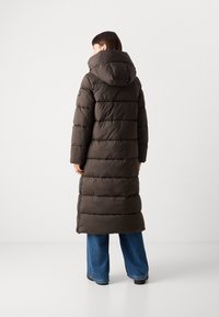 Lange bruine pufferjas met capuchon, met horizontale stiksels, zijknopen en een slim fit over blauwe denim broeken.