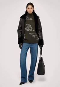 Svart läderjacka med fuskpälskrage, olivgrön tröja med vita linjemönster, blå vida jeans, svarta handskar och väska.