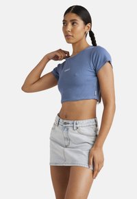T-shirt côtelé bleu raccourci à manches courtes avec logo sur le devant. Associé à une jupe mini en denim bleu clair avec fermeture à boutons sur le devant.
