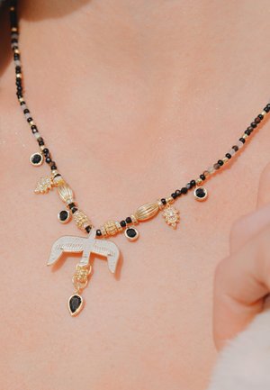 Collier en or orné de perles noires, avec des éléments décoratifs tels qu'un pendentif en forme d'outil de mesure en argent et divers accents en or.
