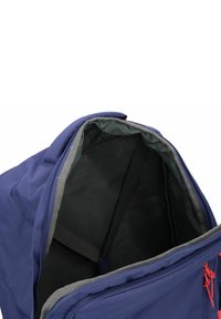 Zaino blu con apertura a cerniera. L'interno presenta una fodera grigia e una cinghia per tenere gli oggetti in posizione. Piccolo dettaglio con cerniera rossa.