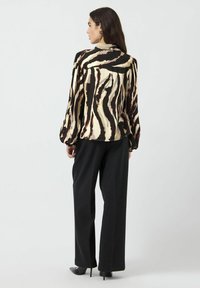 Langermet bluse med et beige og svart zebra-stripes mønster, laget av lett stoff, kombinert med svarte vide bukser og sko med høye hæler.