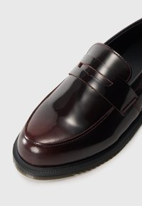 Mocassino in pelle bordeaux con finitura lucida, caratterizzato da un dettaglio a striscia, punta arrotondata e suola in gomma nera testurizzata.