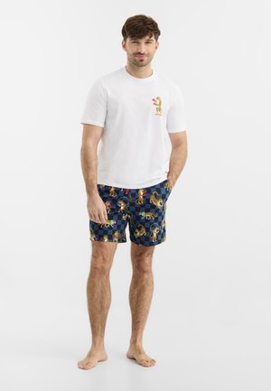 Mand iført hvid T-shirt med lille leopardgrafik og marineblå ternede shorts med forskellige leoparder i forskellige positurer.