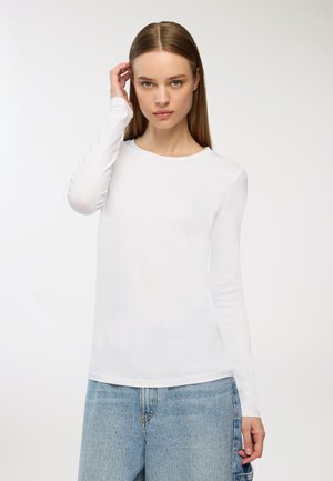 Maglietta bianca a maniche lunghe realizzata in morbido cotone, con scollatura rotonda e design aderente, abbinata a jeans azzurri a vita alta.