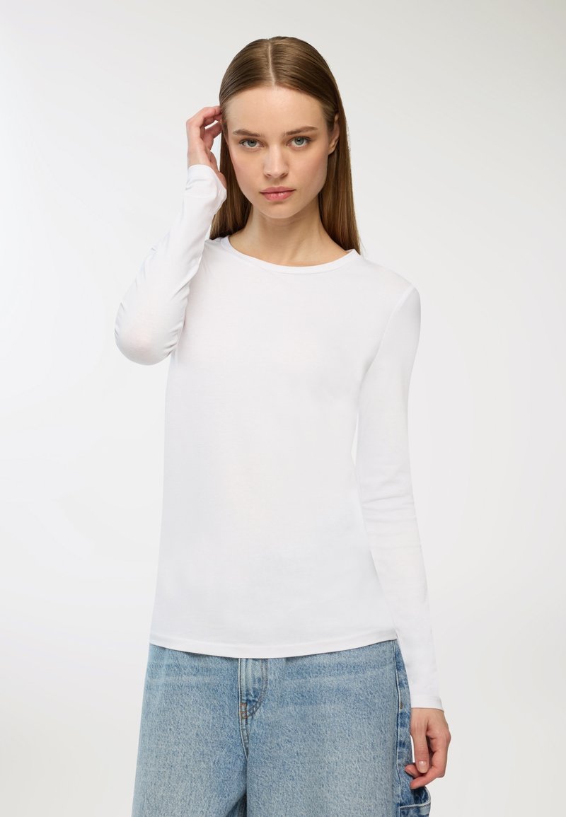 Maglietta bianca a maniche lunghe realizzata in morbido cotone, con scollatura rotonda e design aderente, abbinata a jeans azzurri a vita alta.