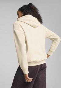 Beige hoodie med en blød tekstur, oversized pasform og stor hætte. Har ribbede manchetter og kant, båret med mørke bukser. Subtil detaljering på ryggen.