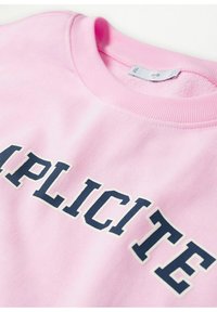 Sweatshirt rose clair avec lettres audacieuses bleu foncé formant le mot "EXPLICITE" sur la poitrine et un col rond côtelé.