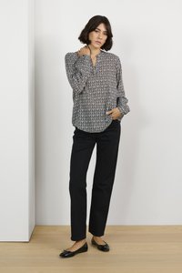 Blusa a maniche lunghe a stampa bianco e nero, abbinata a pantaloni neri e scarpe basse nere, posata su uno sfondo bianco.