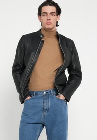 Μαύρο δερμάτινο μπουφάν τύπου bomber με φερμουάρ μπροστά, συνδυασμένο με καφέ ζιβάγκο πουλόβερ και μπλε τζιν, με άνετη εφαρμογή και κλασικό σχέδιο.