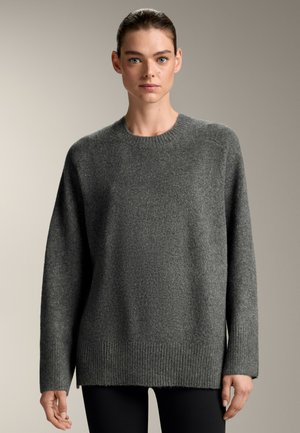 Maglione grigio lavorato a maglia con collo a giro, spalle scese e orlo a costine. Tessuto morbido, vestibilità leggermente oversize, abbinato a leggins neri.
