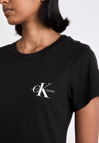 Black cotton t-shirt featuring a round neckline and short sleeves. White logo with "Calvin Klein Jeans" printed in a sleek font on the chest.