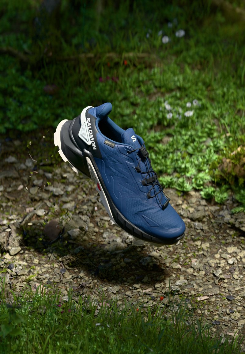 Baskets de course bleues avec une tige synthétique texturée, accents noirs et semelle blanche, dotées d'un système de laçage et d'un logo sur le côté.