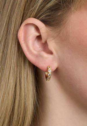 Close-up of a left ear with straight blonde hair, wearing a small gold hoop earring set with three clear gemstones.