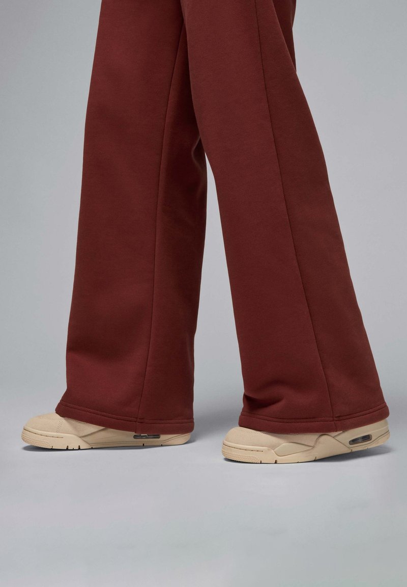 Burgunderfarbene Sweatpants mit lockerer Passform, kombiniert mit beigen Sneakers, die über eine sichtbare Air-Dämpfung und strukturierte Sohlen verfügen.