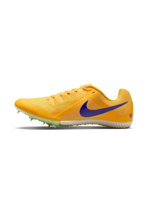 Chaussure de sport jaune avec une tige en mesh, un logo Nike violet, des accents orange et une semelle extérieure verte équipée de pointes métalliques pour l'adhérence.