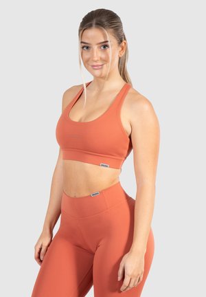 Oranje sportieve croptop met brede bandjes en logodetail, gecombineerd met hoge taille leggings in bijpassende kleur en gladde textuur.