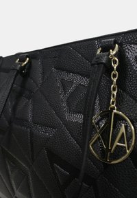Borsa a tracolla nera con texture, caratterizzata da un motivo geometrico, hardware dorato e un charm a forma di "V" attaccato alla tracolla.