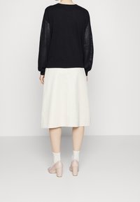 Černý pletený svetr s průhlednými texturovanými rukávy, ve spojení s smetanovou A-liniovou sukní a světle růžovými botami na blokovém podpatku.